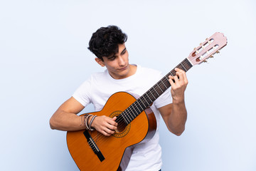 Obraz premium Young Argentinian man with guitar over isolated blue background