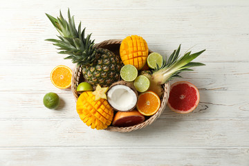Wicker basket with exotic fruits on white wooden background, top view and space for text