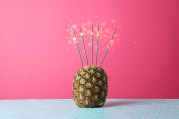Pineapple with burning sparklers on blue table, space for text