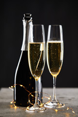 sparkling wine in glasses and bottle with yellow christmas lights, on black