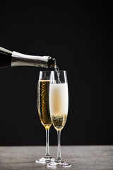 sparkling wine pouring from bottle into glasses for celebrating christmas on black