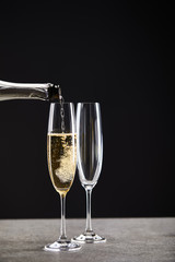 close up of champagne pouring from bottle into glasses for celebrating christmas on black