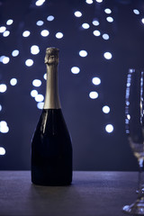 selective focus of champagne bottle and glass with christmas lights bokeh