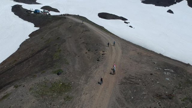 A group of tourists walks along the path leading to the Avachinsky volcano, Kamchatka, Russia. Video shooting from a drone. Snowy landscape.