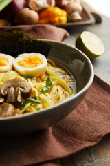 close up view of traditional spicy ramen in bowl on brown napkin on stone surface