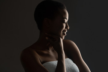 Fototapeta na wymiar Portrait of beautiful african girl wrapped in towel, standing in darkness