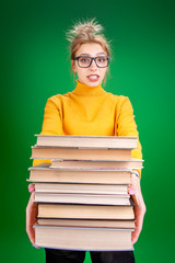 blonde girl in a yellow sweater holds a stack of books on a green background