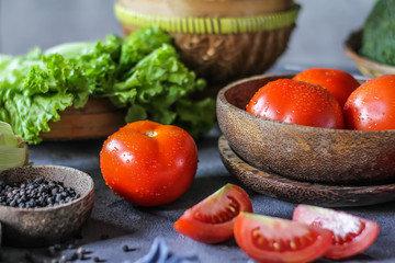 Photo of fresh tomatoes in a bowl on dark background around vegetables, carrot, salt, black pepper, corn, broccoli. Slice tomatoes. Harvesting tomatoes. Drops of water vegetables. Wooden table. Image