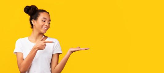 Satisfied black teen pointing with finger at copy space