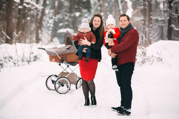 A beautiful family with retro pram walks through the winter snowy forest. Mother, father, daughter and baby son enjoying day outdoors. Holidays, christmas, happiness together, childhood in love.