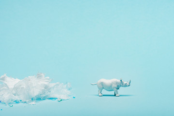 White rhinoceros toy and plastic garbage on blue background, animal welfare concept