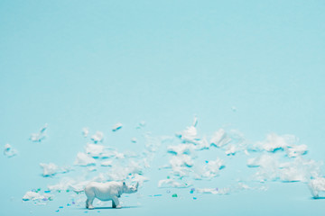 White rhinoceros toy and plastic garbage on blue background, environmental pollution concept
