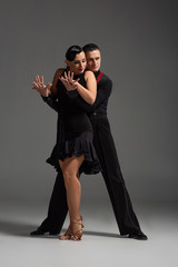 elegant couple of dancers in black clothing performing tango on grey background