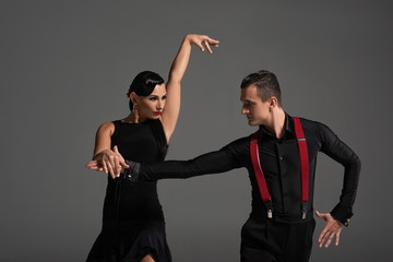 elegant couple of dancers looking at each other while performing tango isolated on grey