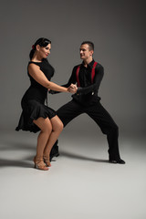 two smiling dancers in black clothes performing tango on grey background