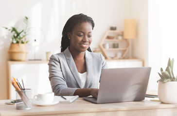 Smiling afro businesswoman working on laptop in modern office