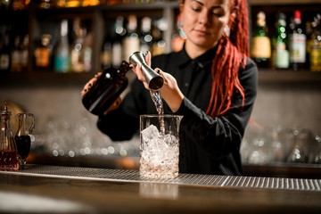 Bartender girl pouring a alcoholic drink from the jigger to a measuring glass cup