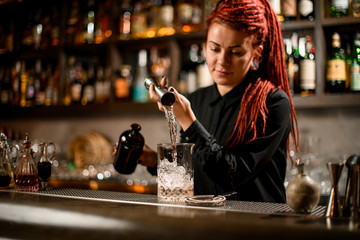 Professional bartender girl pouring a alcoholic drink from the jigger to a measuring glass cup