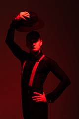 expressive tango dancer looking at camera and holding hat above head on dark background with red lighting