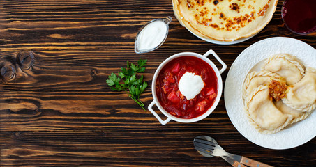 The concept of Eastern European national cuisine. Ukrainian, Russian, Polish food.Traditional beetroot soup Borscht with sour cream, pancakes Blini, dumplings Vareniki with potatoes and fried onions