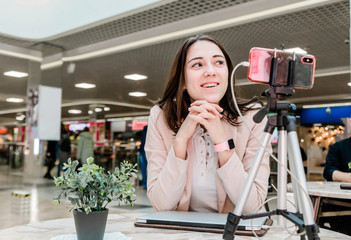 A young woman blogger in a shopping center works at a laptop, conducts live broadcasts, records videos, communicates with followers of her social networks