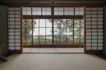 View of green trees and Kyoto from a window in a traditional room with shoji dividers and tatami in...