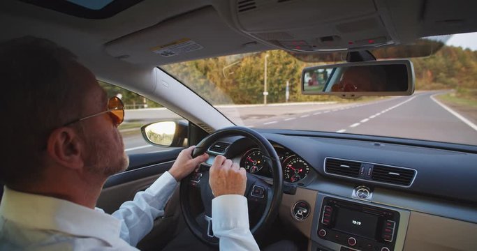 Adult bearded man driving elegant auto tapping finger over the steering wheel. Footage for animation. Business class lifestyle. Round sunglasses. Sunny background. Classic casual fashion. Application