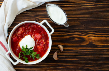 Borscht traditional beetroot soup, Ukrainian and Russian national cuisine. Borsch served in a white bowl with sour cream and parsley on a wooden table. Top view, flat lay