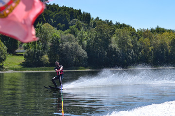 Young man water skiing over the river in summer, having fun