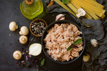 Fresh minced meat and ingredients for cooking - mushrooms, pasta, spices and eggs on a dark stone countertop. Top view on a flat background lay.