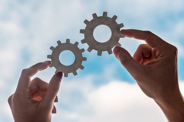 cropped view of man and woman holding gears on blue sky background