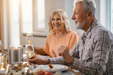 Happy senior woman enjoying in glass of wine during lunch time at home.