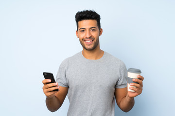Young handsome man over isolated background holding coffee to take away and a mobile