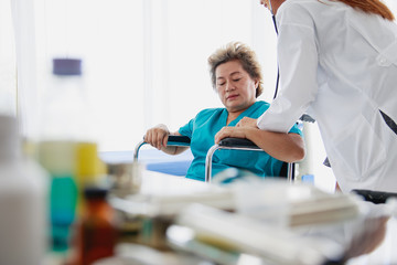 Elderly female patients sit in wheelchairs for female doctors to use stethoscope to listen to the heartbeat.