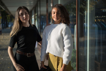 Portrait of a pair of beautiful Hispanic girls at the store counter. Girls point their finger at the counter with clothes. One of the women in a black hat. Fashion photography