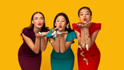 Three Girls In Dresses Blowing Confetti From Hands In Studio