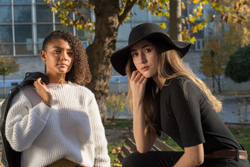 Portrait of two beautiful mexican millennial generation girls. Autumn fashion photo shoot in the park by the bench.