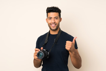Young handsome man over isolated background with a professional camera and with thumb up
