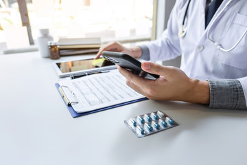 Doctor working and using smartphone note information on paper report in hospital and medical stethoscope, medicine on clipboard on desk