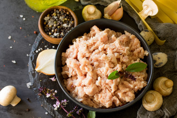 Fresh minced meat and ingredients for cooking - mushrooms, pasta, spices and eggs on a dark stone countertop.