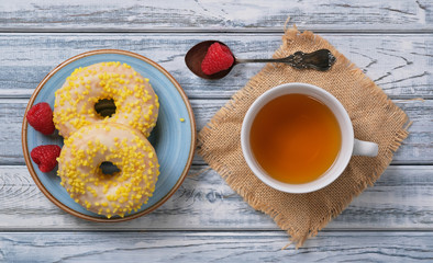Sweet yellow donuts with white sprinkles on blue glazed saucer. Dessert with tasty, delicious doughnuts, silver old teaspoon, cup of green chamomile tea, berries of fresh juicy raspberries. Top view.