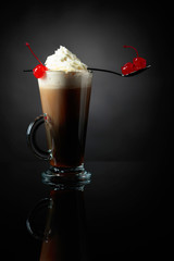 Layered coffee cocktail with whipped cream and red cherry.