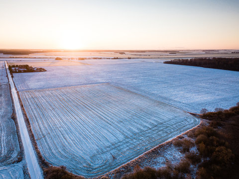 Aerial view of agricultural fields covered in first snow - Early winter scenery with sunrise in background