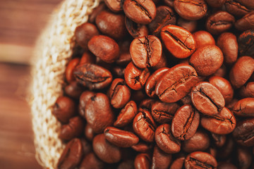 Coffee beans closeup in burlap bag on wooden background. Soft contrast. Aromatic roasted coffee beans.