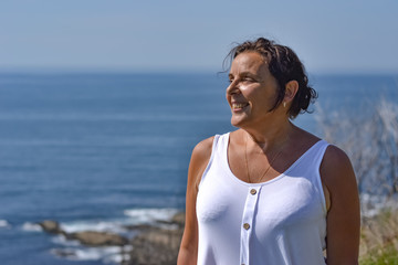 Middle age woman portrait by the sea side in summer, smiling