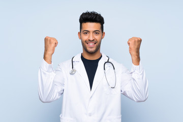 Young doctor man over isolated blue wall celebrating a victory