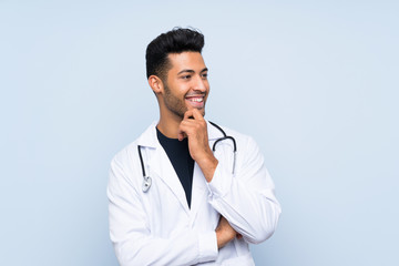 Young doctor man over isolated blue wall looking side