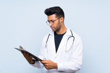 Young doctor man over isolated blue wall