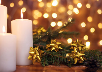 Fototapeta na wymiar Golden Christmas ball on a tree branch, white candle flame with stars bokeh lights on a brown background