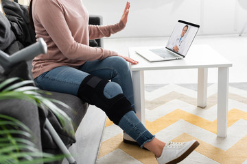 cropped view of woman with broken leg having online consultation with doctor on laptop at home - Powered by Adobe